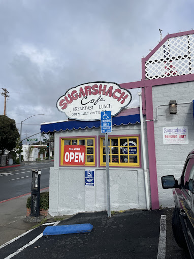 Sugar Shack Cafe storefront with its blue scalloped awning and red OPEN flag on a sunny day